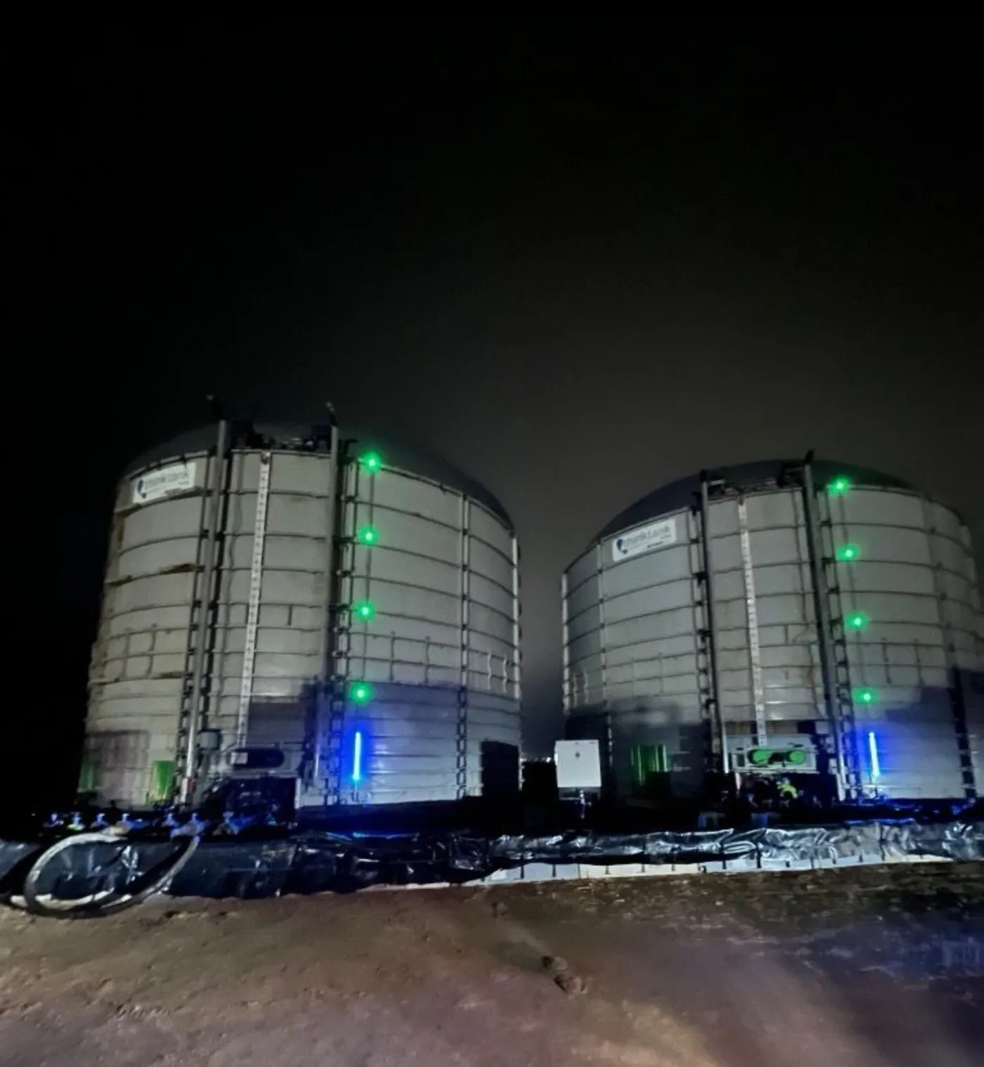 Storage tanks at night lit by SHIELD blue and green LED level bars